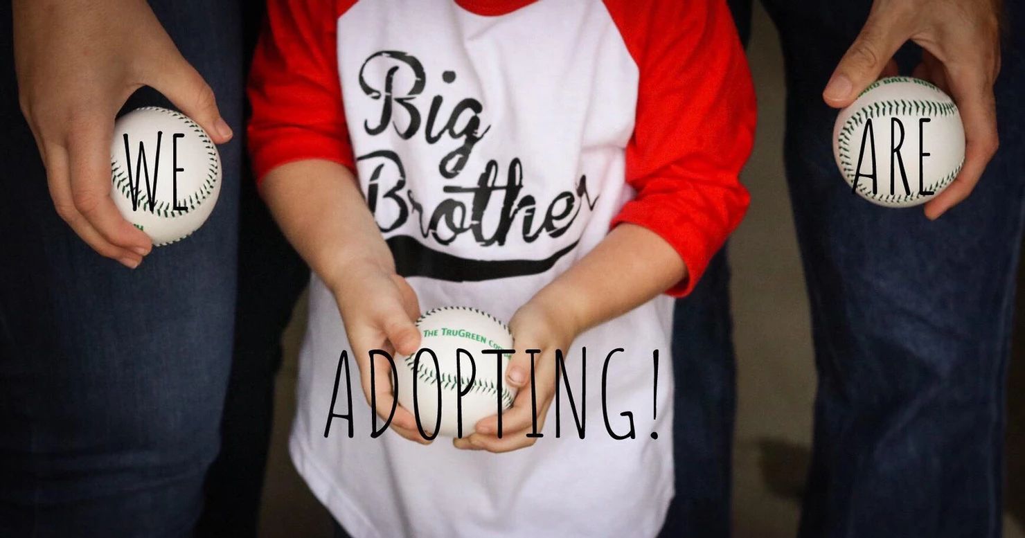 A Family Holding a we are Adopting Sign